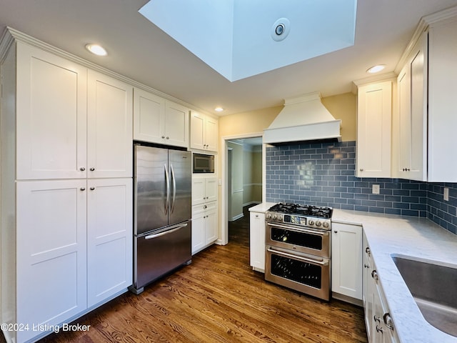 kitchen with appliances with stainless steel finishes, tasteful backsplash, custom exhaust hood, dark wood-type flooring, and white cabinets