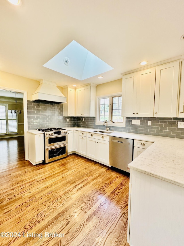 kitchen with premium range hood, sink, light hardwood / wood-style floors, white cabinetry, and stainless steel appliances