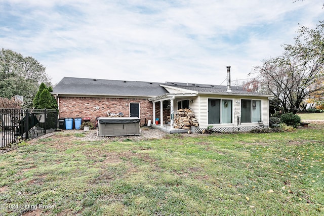 rear view of property featuring a hot tub and a lawn