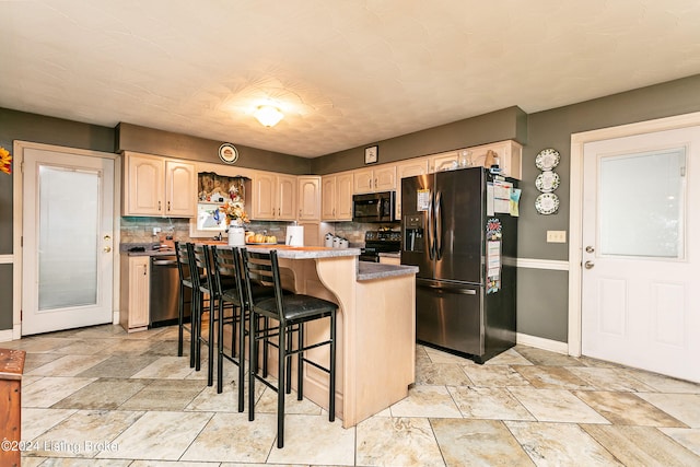 kitchen with a kitchen bar, a center island, backsplash, light brown cabinets, and appliances with stainless steel finishes