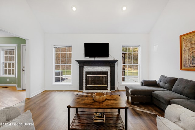 living room with vaulted ceiling, a stone fireplace, and dark hardwood / wood-style flooring