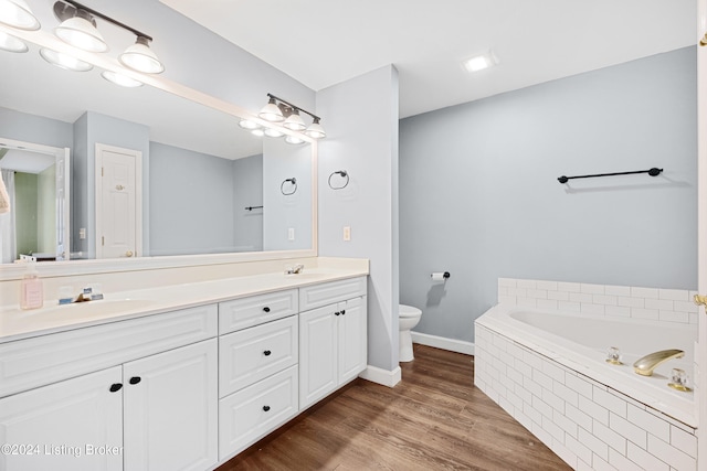 bathroom with hardwood / wood-style flooring, vanity, toilet, and tiled bath