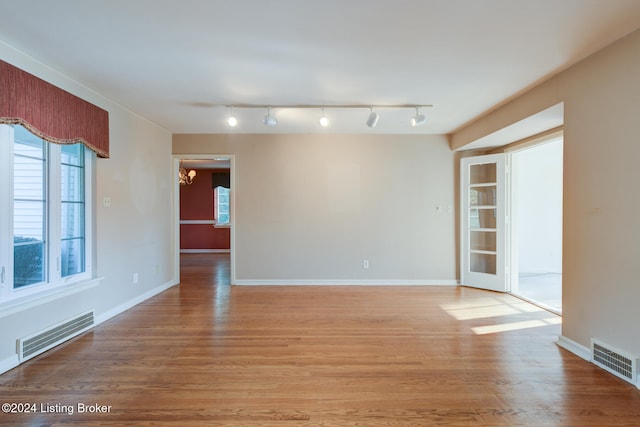 unfurnished room with light hardwood / wood-style floors, rail lighting, and a notable chandelier