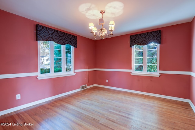 empty room featuring plenty of natural light, wood-type flooring, and a notable chandelier