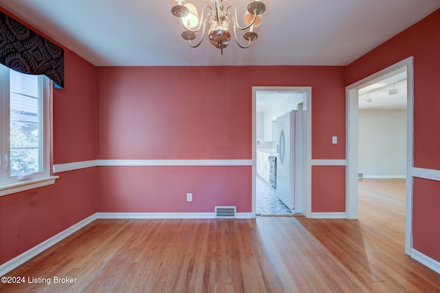 spare room featuring light wood-type flooring and an inviting chandelier