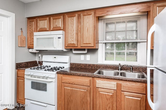 kitchen with dark stone counters, white appliances, sink, and plenty of natural light