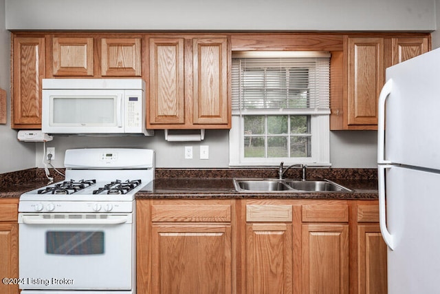 kitchen featuring white appliances, dark stone countertops, and sink