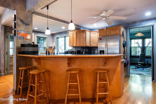 kitchen with light hardwood / wood-style floors, kitchen peninsula, stainless steel fridge with ice dispenser, a kitchen breakfast bar, and ceiling fan