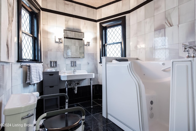 bathroom with tile walls, a wealth of natural light, a tub to relax in, and sink