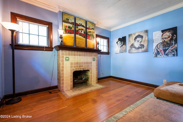 unfurnished living room featuring a tiled fireplace, a textured ceiling, hardwood / wood-style flooring, and crown molding