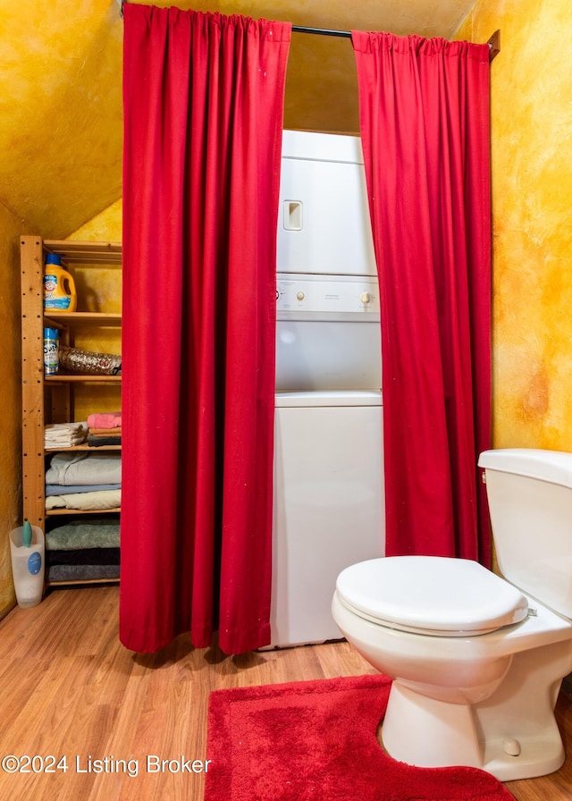 bathroom featuring toilet, stacked washer and clothes dryer, and hardwood / wood-style flooring