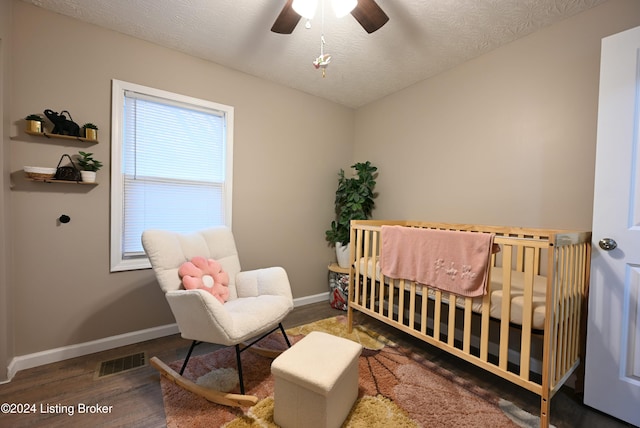 bedroom with ceiling fan, a textured ceiling, dark hardwood / wood-style floors, and a crib