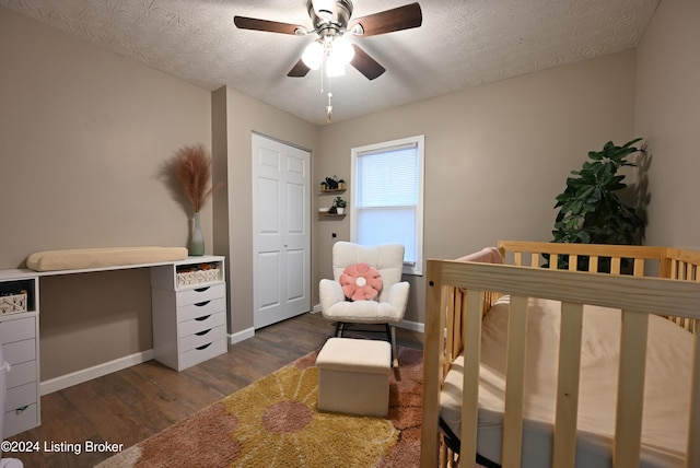 bedroom with a crib, a textured ceiling, dark hardwood / wood-style floors, and ceiling fan