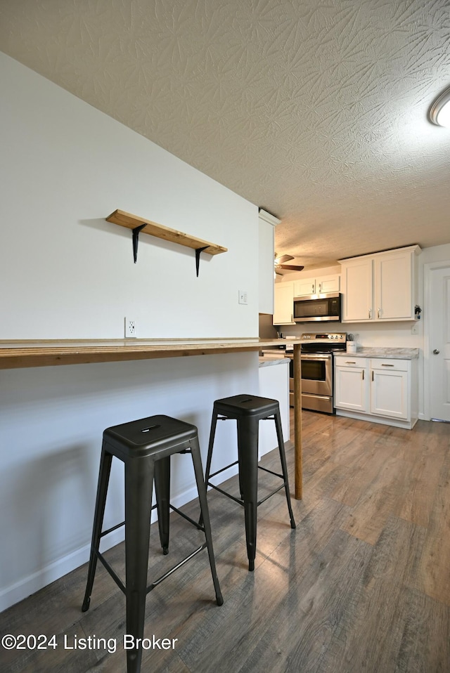 kitchen featuring dark wood-type flooring, white cabinets, a breakfast bar area, a textured ceiling, and appliances with stainless steel finishes