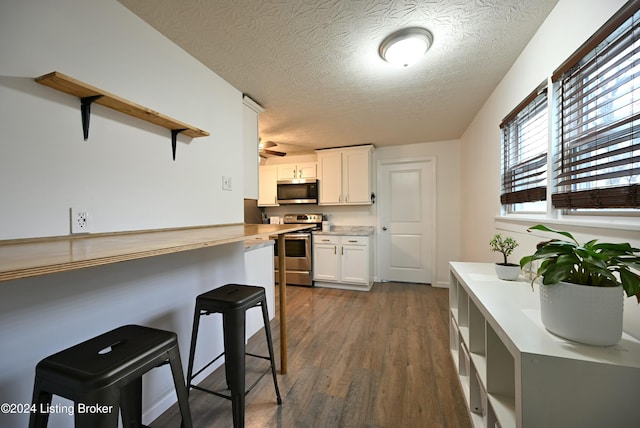 kitchen featuring dark hardwood / wood-style flooring, a textured ceiling, a breakfast bar area, white cabinetry, and appliances with stainless steel finishes