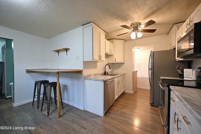 kitchen with sink, appliances with stainless steel finishes, a textured ceiling, white cabinets, and dark hardwood / wood-style flooring