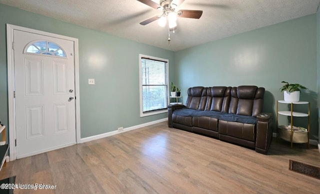 living room with light hardwood / wood-style floors, ceiling fan, and a textured ceiling