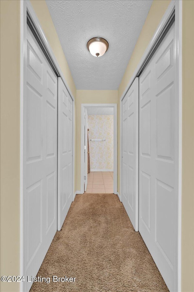 hall with a textured ceiling and light carpet