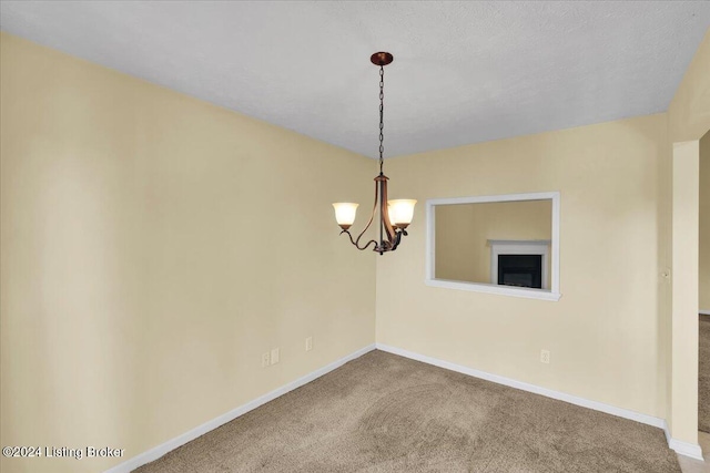 carpeted empty room featuring a textured ceiling and an inviting chandelier