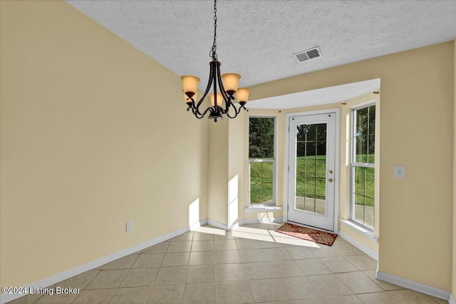 unfurnished dining area featuring an inviting chandelier, a textured ceiling, and light tile patterned floors