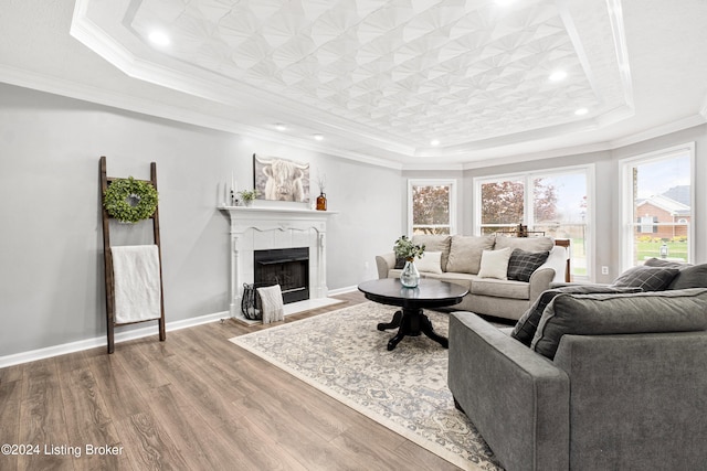 living room with a tile fireplace, wood-type flooring, a raised ceiling, and ornamental molding