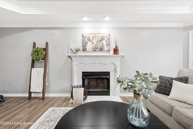 living room with a tile fireplace, wood-type flooring, and ornamental molding