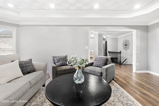 living room with a raised ceiling, wood-type flooring, and ornamental molding