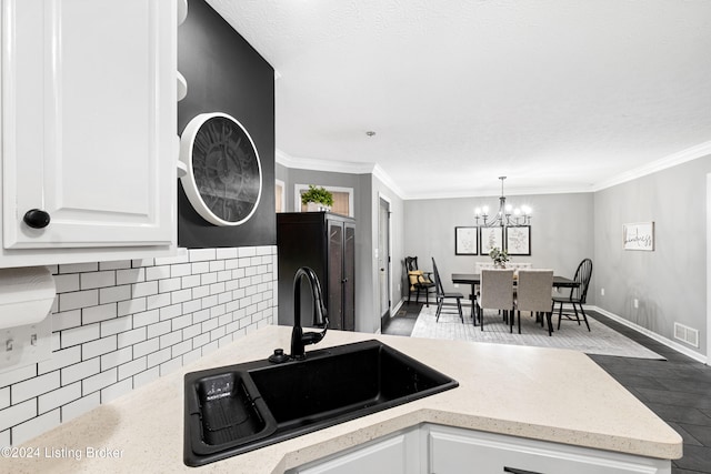 kitchen with ornamental molding, sink, pendant lighting, a notable chandelier, and white cabinets