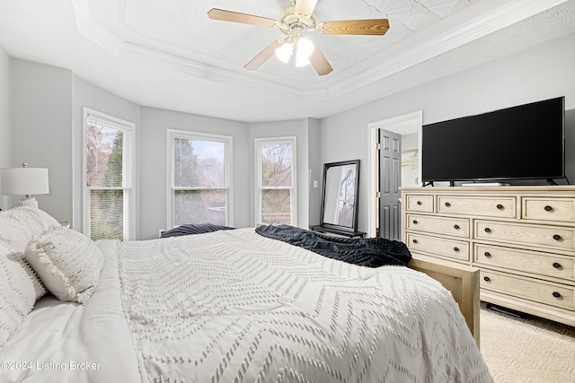 carpeted bedroom with ceiling fan, crown molding, and a tray ceiling