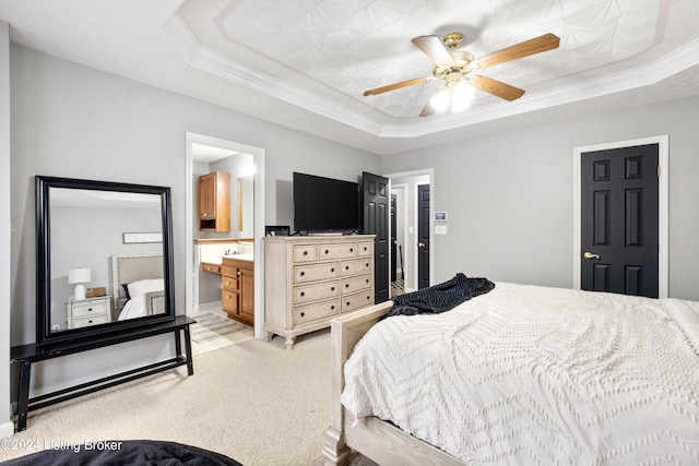 carpeted bedroom with ceiling fan, ornamental molding, a tray ceiling, and ensuite bath