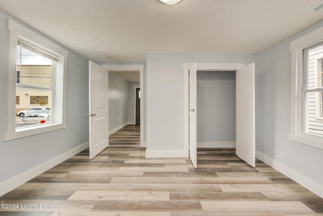 unfurnished bedroom with light wood-type flooring, a textured ceiling, and a closet