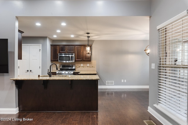 kitchen featuring stainless steel appliances, dark hardwood / wood-style floors, pendant lighting, a breakfast bar area, and kitchen peninsula