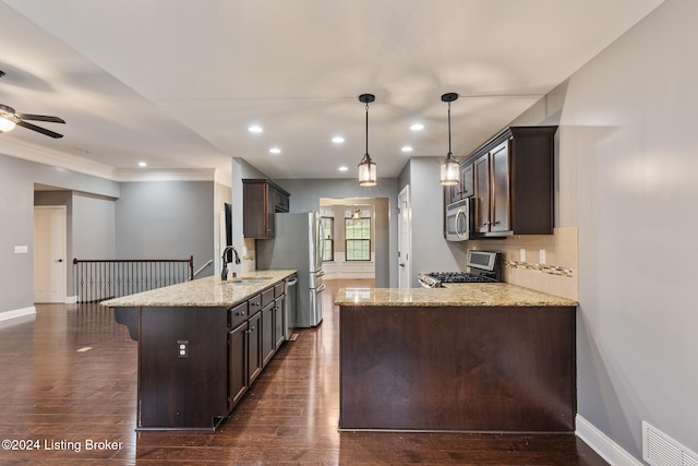 kitchen with appliances with stainless steel finishes, pendant lighting, light stone countertops, sink, and kitchen peninsula