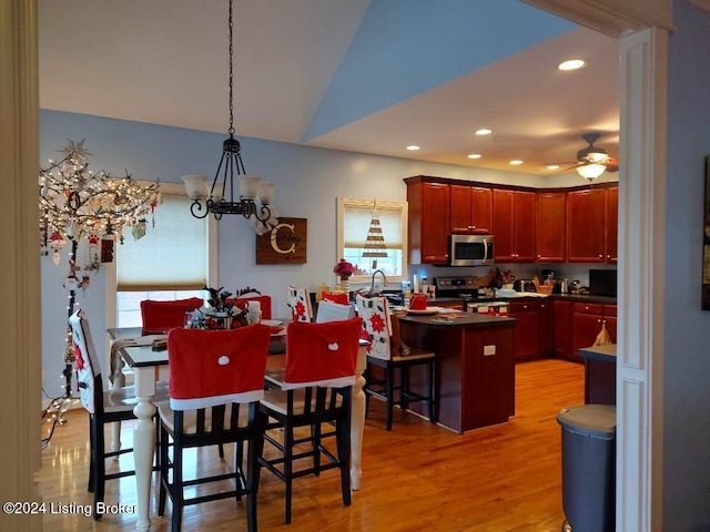 kitchen with ceiling fan with notable chandelier, stainless steel appliances, light hardwood / wood-style flooring, hanging light fixtures, and a breakfast bar area