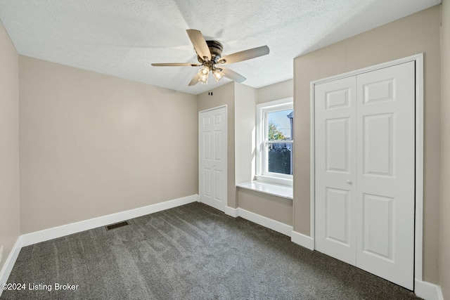 unfurnished bedroom with ceiling fan, dark colored carpet, and a textured ceiling