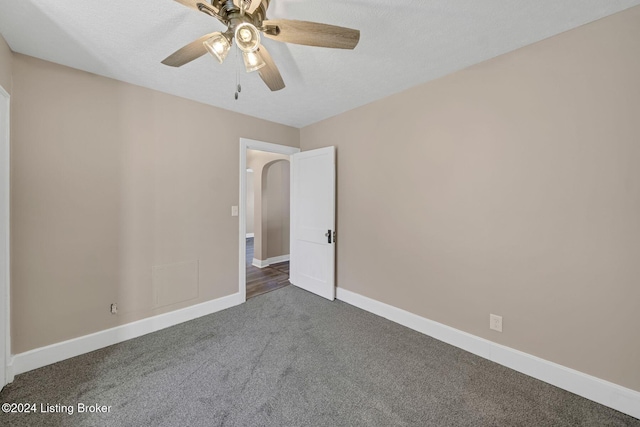 spare room featuring a textured ceiling, dark colored carpet, and ceiling fan