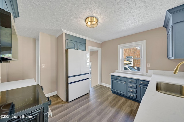 kitchen featuring light wood-type flooring, white refrigerator, a textured ceiling, stove, and sink