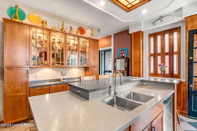 kitchen featuring stainless steel dishwasher, sink, a kitchen island with sink, and decorative backsplash