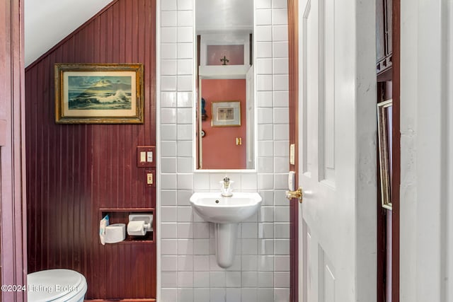 bathroom featuring wooden walls, toilet, and tile walls