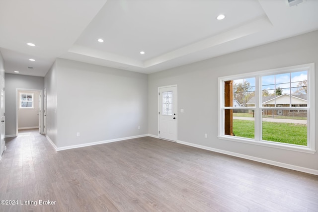 unfurnished living room with a wealth of natural light, light hardwood / wood-style floors, and a tray ceiling