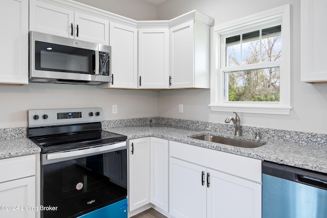 kitchen with white cabinetry, stainless steel appliances, sink, and light stone counters