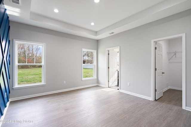 unfurnished bedroom featuring light hardwood / wood-style floors, multiple windows, a closet, and a walk in closet