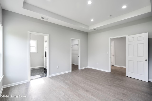 unfurnished bedroom featuring ensuite bathroom, hardwood / wood-style floors, a walk in closet, and a closet