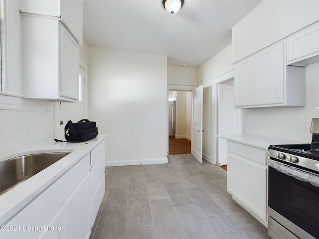 kitchen featuring white cabinets, decorative backsplash, stainless steel stove, and light hardwood / wood-style floors