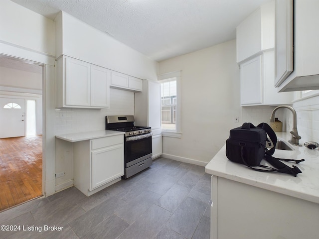 kitchen featuring stainless steel gas range oven, white cabinets, decorative backsplash, light wood-type flooring, and a textured ceiling