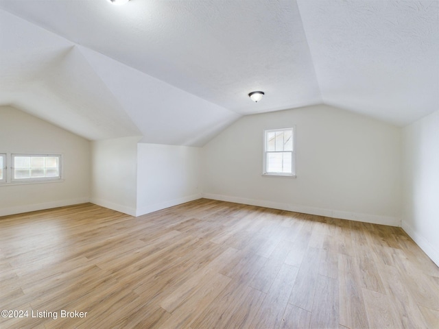 bonus room featuring a textured ceiling, light wood-type flooring, and lofted ceiling