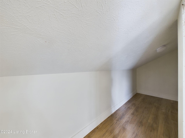 additional living space with a textured ceiling, wood-type flooring, and lofted ceiling