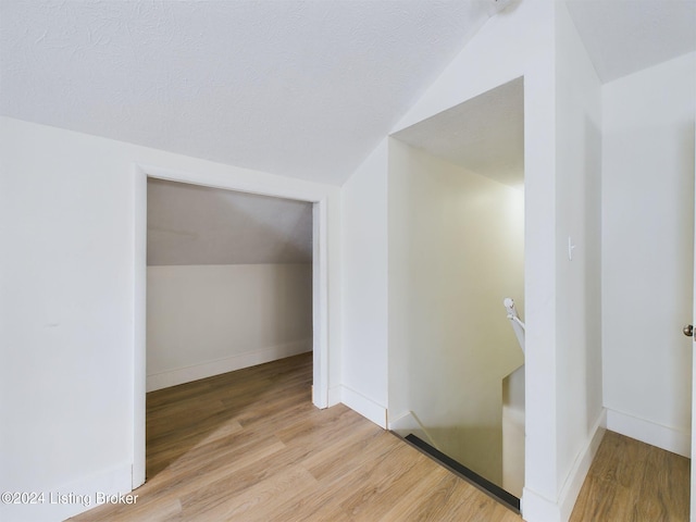 hallway featuring a textured ceiling, light hardwood / wood-style floors, and lofted ceiling