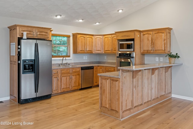 kitchen with appliances with stainless steel finishes, light stone countertops, sink, light hardwood / wood-style floors, and kitchen peninsula