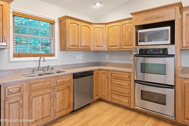 kitchen featuring stainless steel appliances, sink, light stone counters, light hardwood / wood-style flooring, and vaulted ceiling